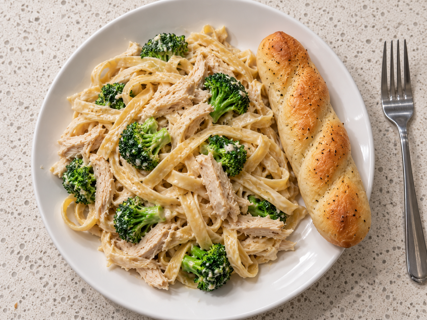 Easy chicken broccoli Alfredo served on a white plate with a garlic breadstick